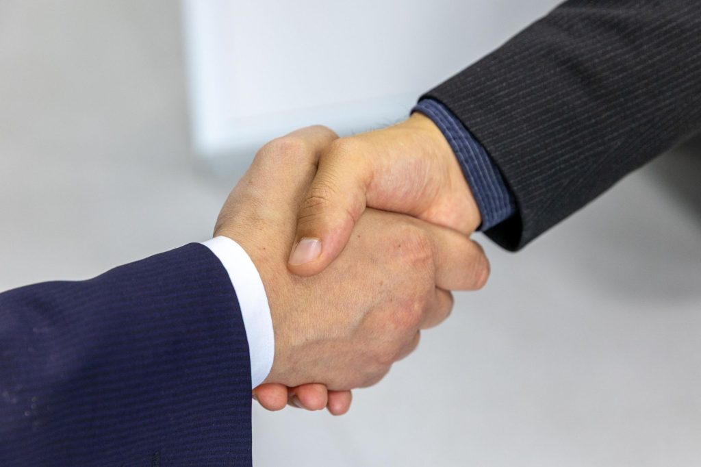 Poignée de main professionnelle entre deux personnes en costume, illustrant les façades sociales du monde du travail