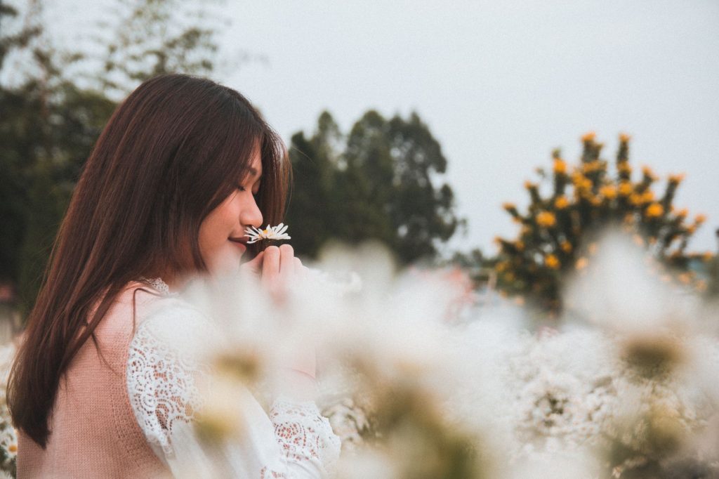 Une femme respire le parfum d'une fleur, les paupières baissées