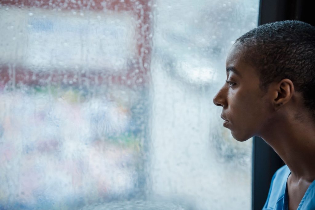 Femme pensive assise près d’une fenêtre, le regard perdu, illustrant les ruminations du deuil