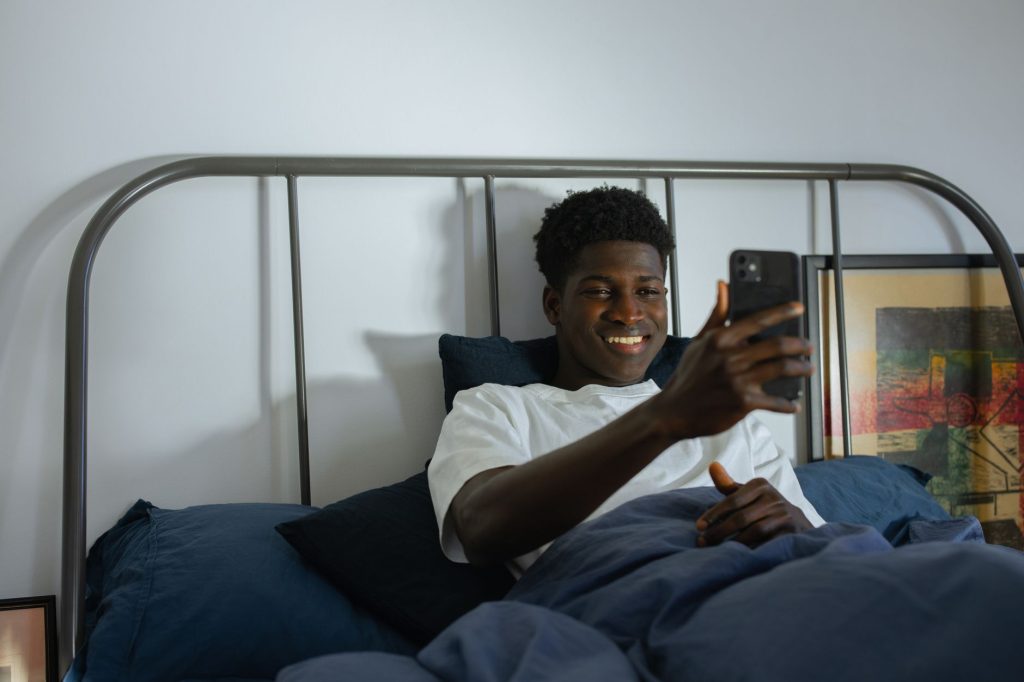 Une femme souriante lit un message sur son téléphone, allongée sur son lit