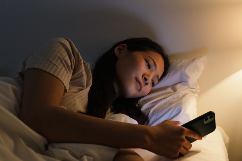 Une femme consulte discrètement son téléphone près d’une fenêtre, le soir